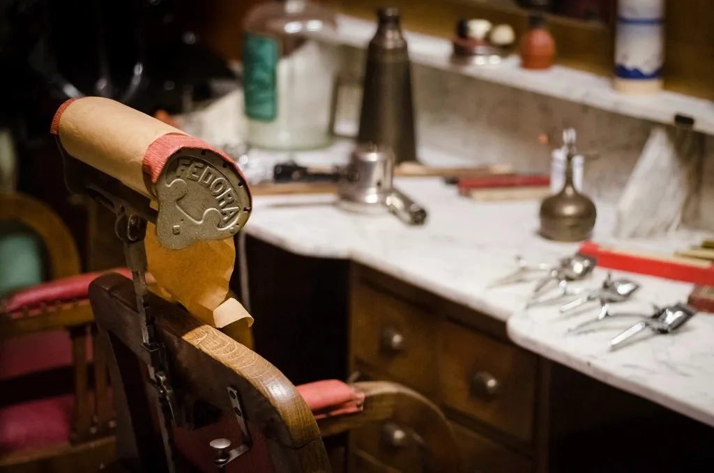 A vintage barber's chair beside a marble counter laid out with scissors and combs