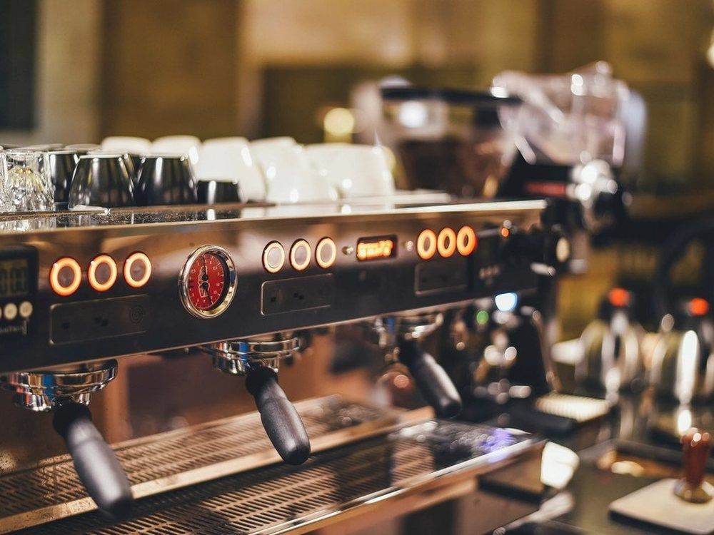 The chrome front of an espresso machine with its gauges lit, cups stacked on top