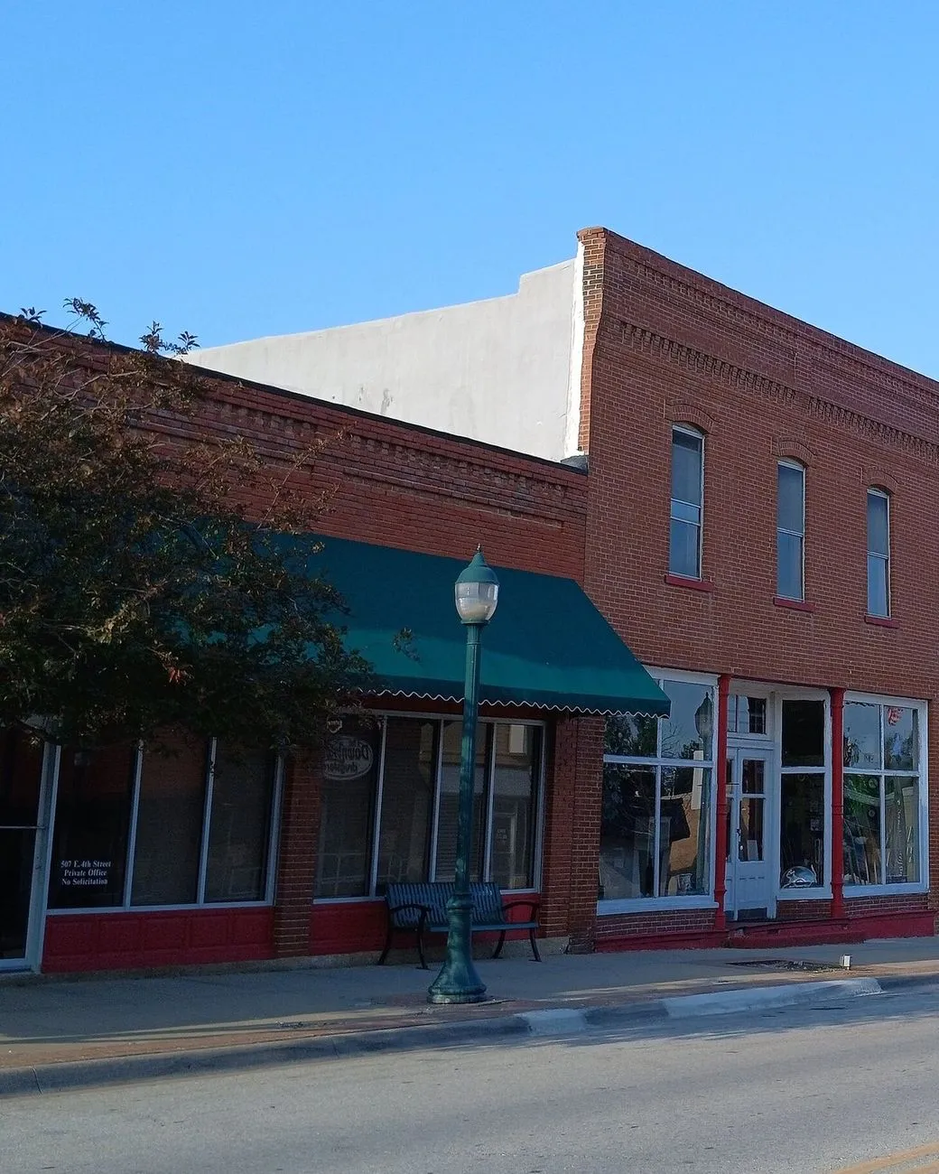 A red-brick storefront with a green awning and tall display windows on a quiet small-town main street